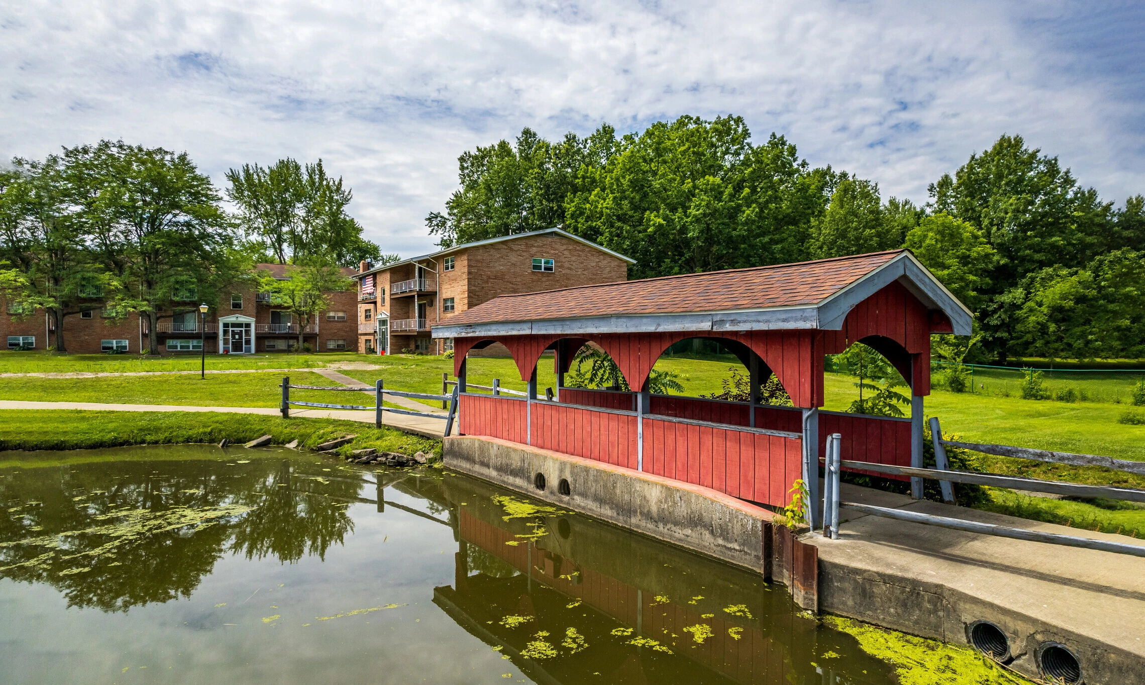 Wide view across the pond toward the covered bridge and apartment buildings under a broad sky.